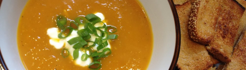 Bowl of homemade pumpkin soup topped with yoghurt and fresh herbs.