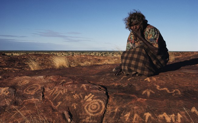 An Aboriginal woman sits by rock carvings in Western Australia. Photograph: Medford Taylor/Getty