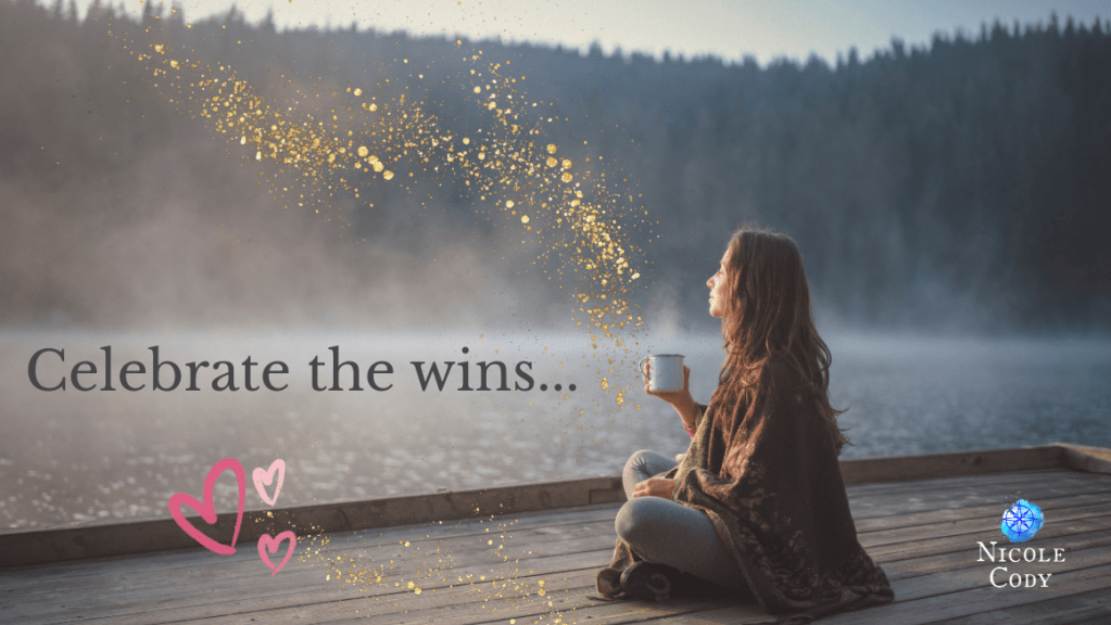 Woman sitting by a lake holding a cup of tea with soft golden light, symbolising celebrating small wins and finding joy in everyday moments.